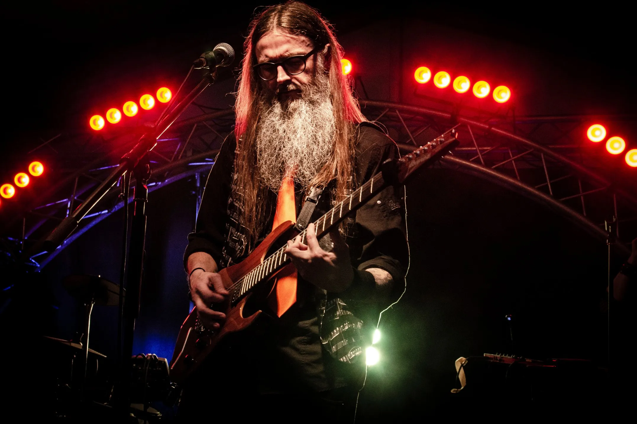 Peter Capon playing guitar live on stage under red lights