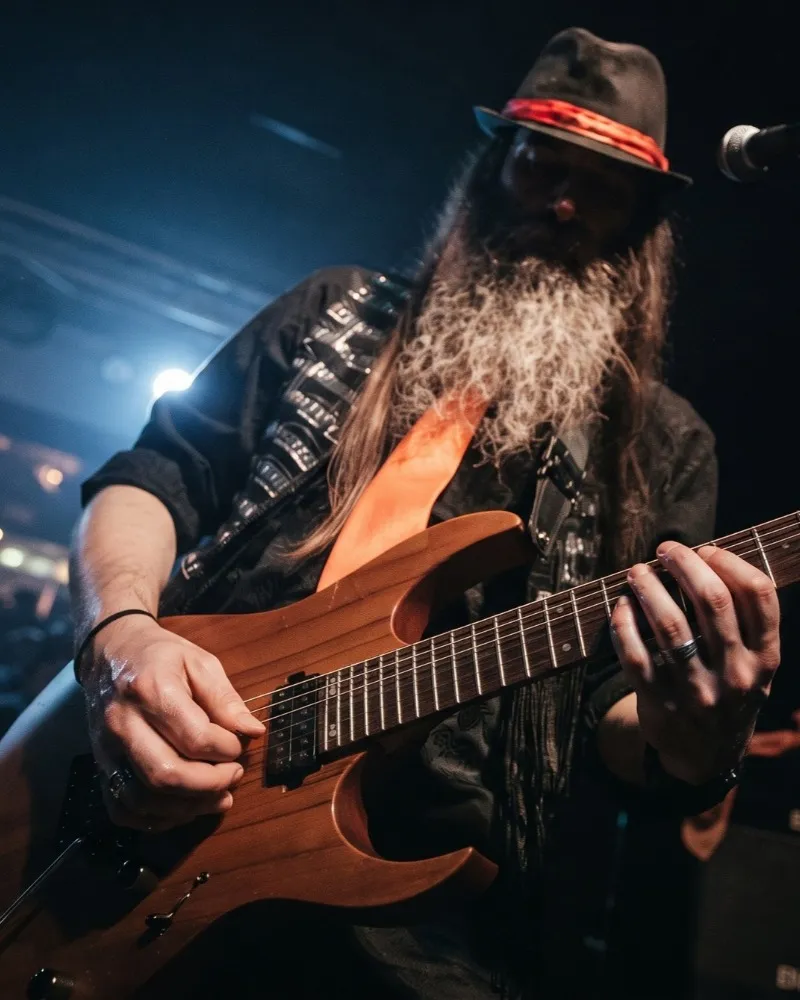 Close-up of Peter Capon in a hat playing guitar live