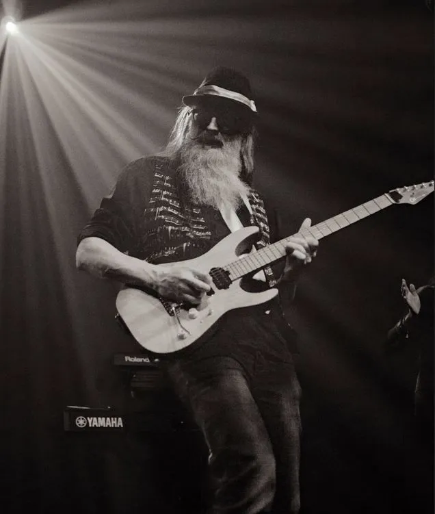 Peter Capon playing guitar live in a spotlight, black and white