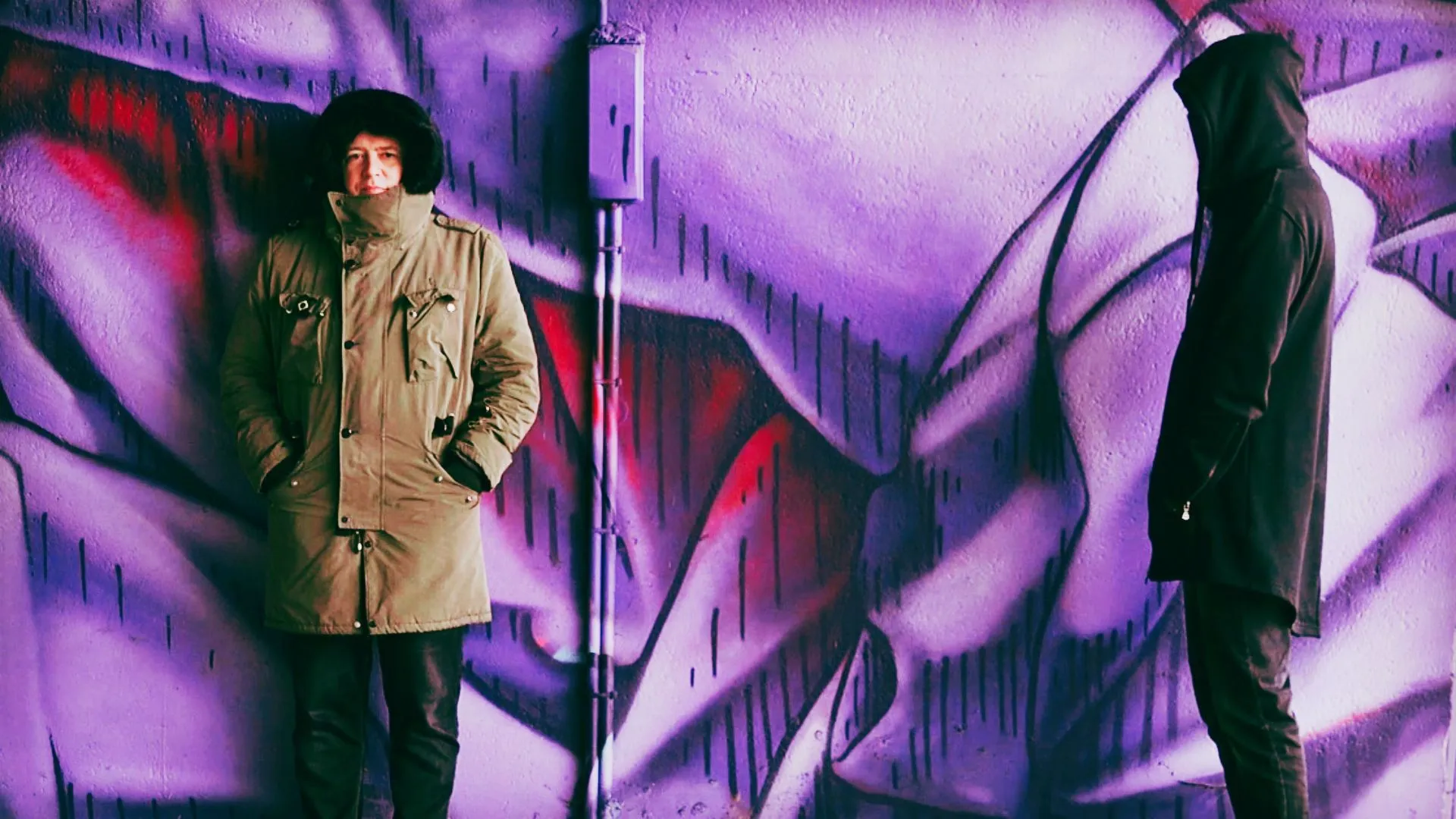 Two figures in front of a purple graffiti wall, from the Scarhead video